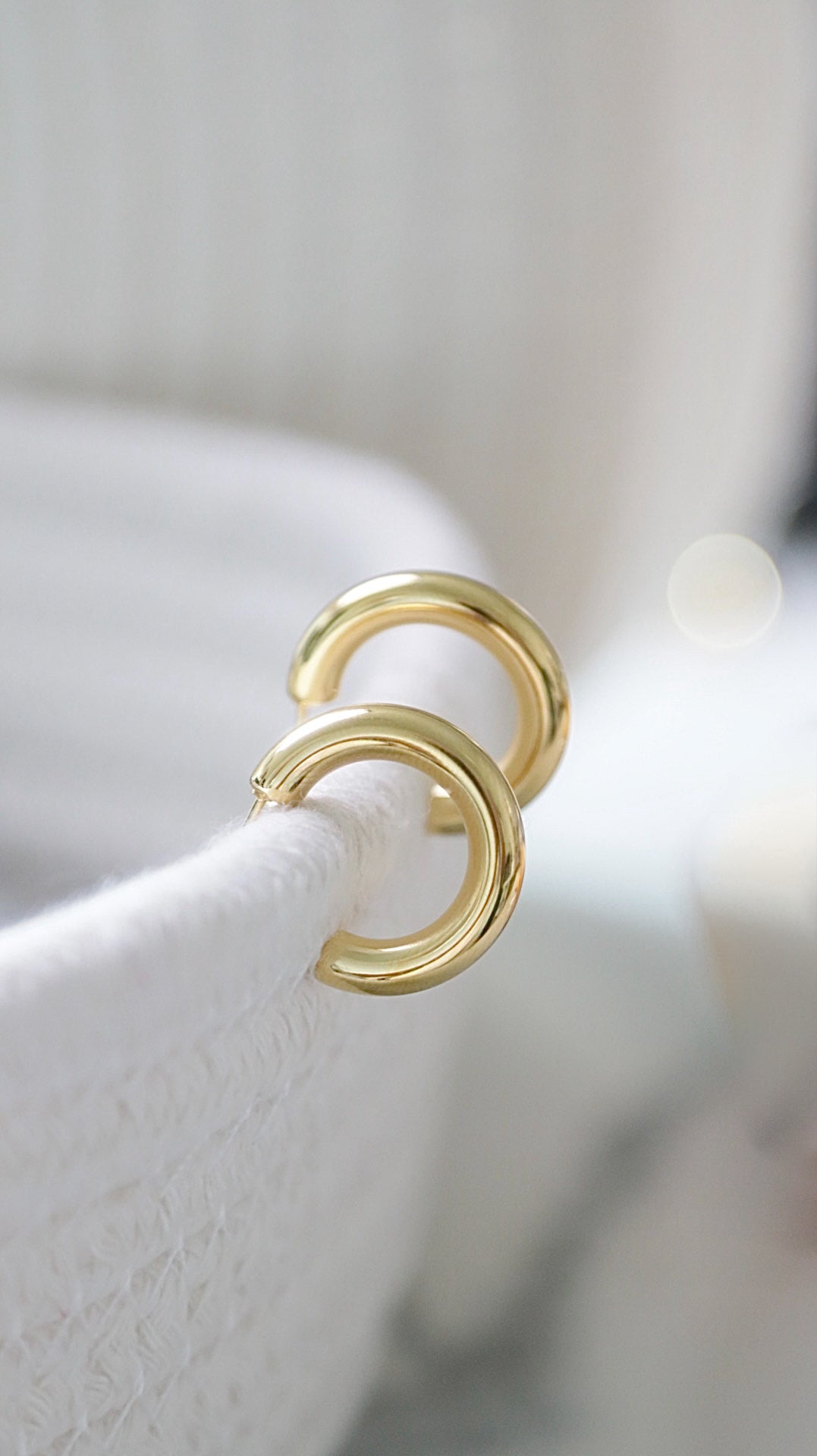 Gold hoop earrings on a white stand with a blurred background